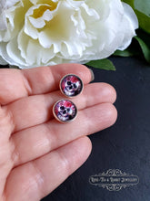 Load image into Gallery viewer, Stud Earrings, Flower Crown Skull, Glass Cabochon, 12mm Diameter, Silver Plated, Sterling Silver Butterfly Closure, Halloween, Gift, held in hand to show dimension perspective